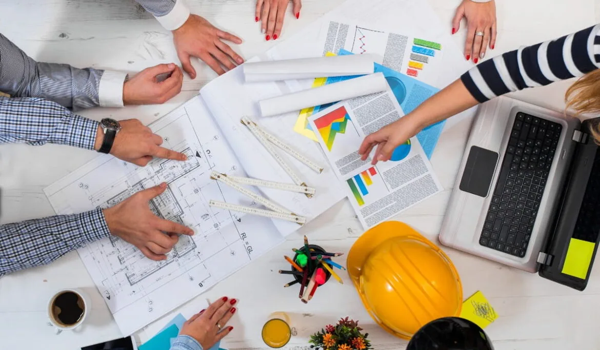 A project management team reviewing architectural blueprints, charts, and schedules, collaborating on construction planning and contractor coordination.